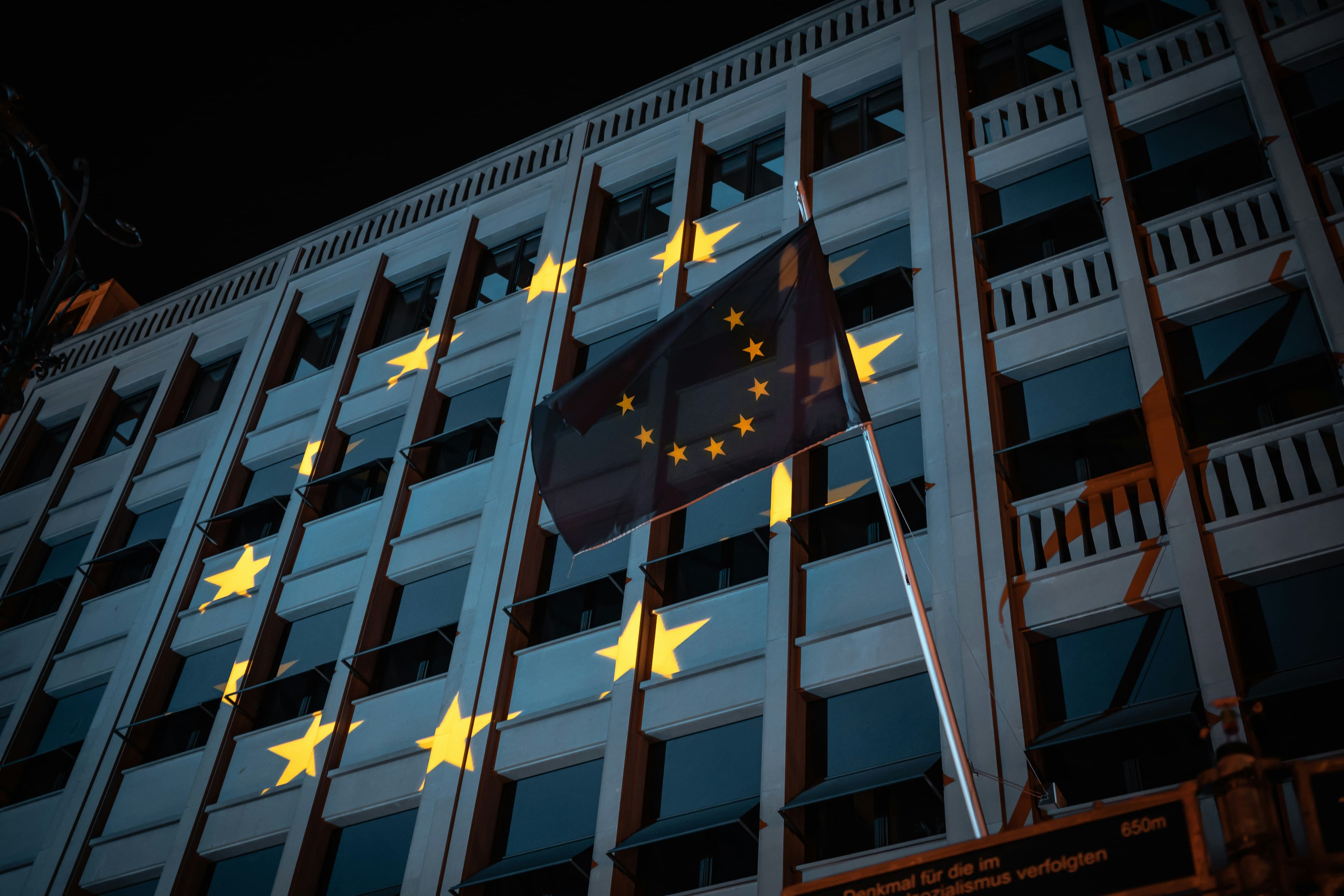 European Union flag outside a European institutional building at night, with yellow stars projected across the facade.